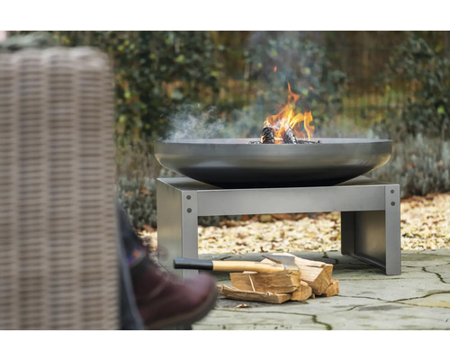 Feuerschale mit Holz auf einem Metallsockel im Garten.