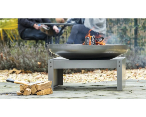 Feuerstelle aus Metall mit brennendem Holz und Holzscheiten im Freien