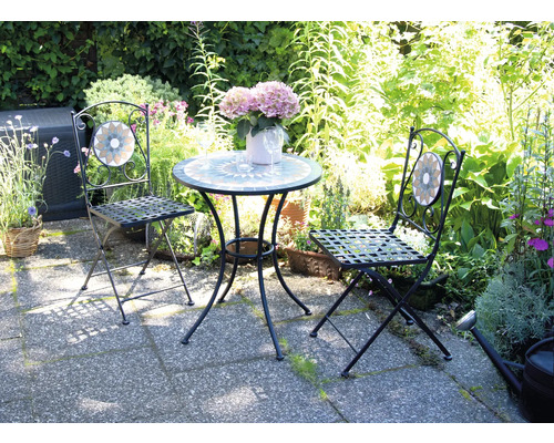 Gartenszene mit Tisch und zwei Stühlen mit Mosaikdetails vor üppigem Grün