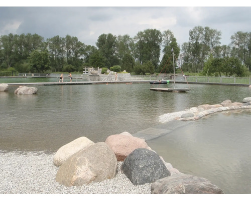 Naturbadesee mit Holzsteg, bepflanztem Ufer und Steinen im Wasser