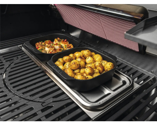 Grill mit Speisen in schwarzen Schalen: Kartoffeln und Meeresfrüchte.