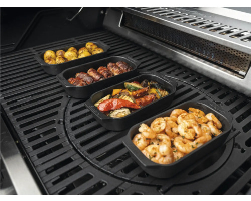 Verschiedene Speisen in Grillpfannen auf einem Grill, darunter Kartoffeln, Fleischröllchen, Gemüse und Garnelen.