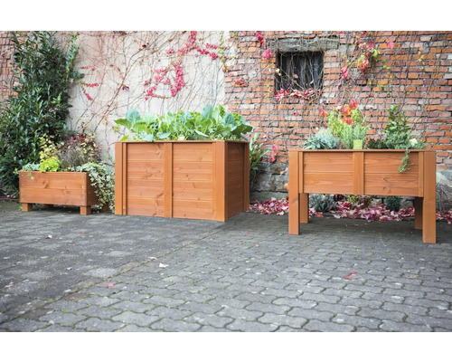 Drei Pflanzkästen aus Holz unterschiedlicher Größe vor einer Backsteinmauer mit Pflanzen