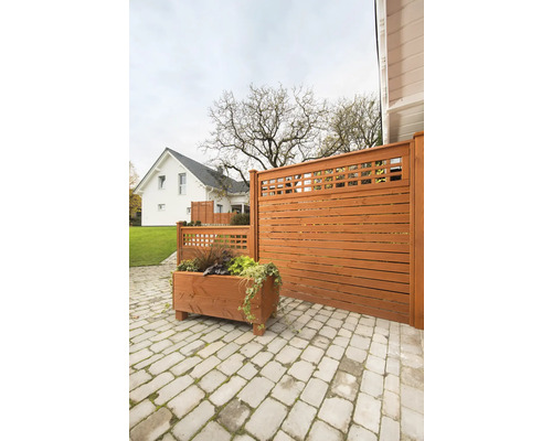 Holzzaun mit Pflanzkasten auf einer gepflasterten Terrasse vor einem Wohnhaus