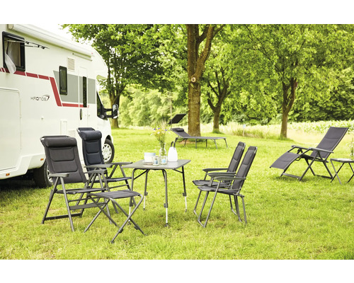 Campingplatzszene mit Wohnwagen, Tisch, Stühlen und Liegestühlen auf einer Wiese