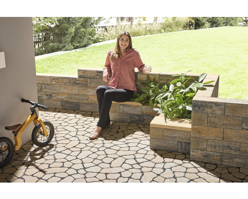 Gartenbereich mit Bodenplatten in Natursteinoptik, Mauer und einer Frau, die auf einer Bank sitzt