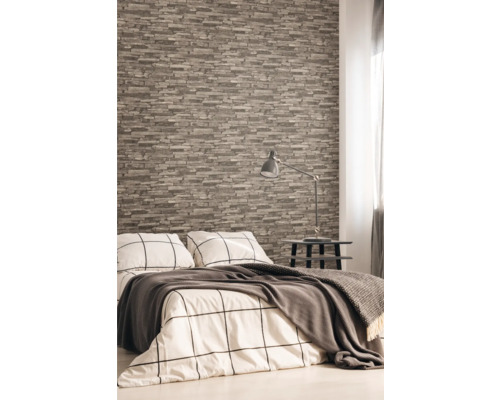 Schlafzimmer mit Steinoptik Tapete, Bett, Nachttisch und Lampe.