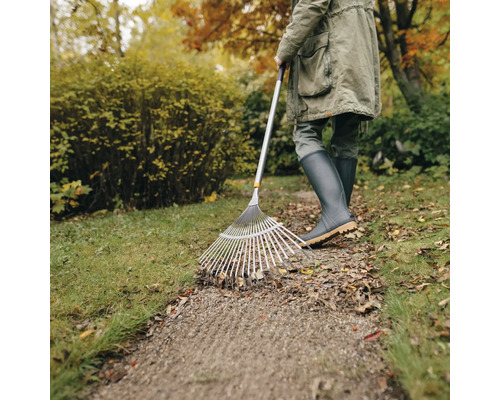 Person harkt Blätter mit einem Laubbesen im Garten.