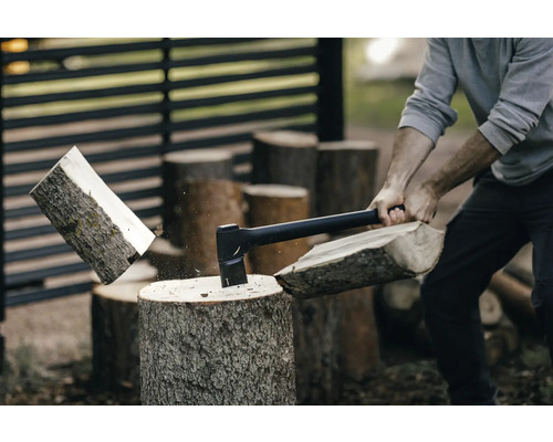 Mann spaltet Holz mit einer Axt auf einem Holzscheit