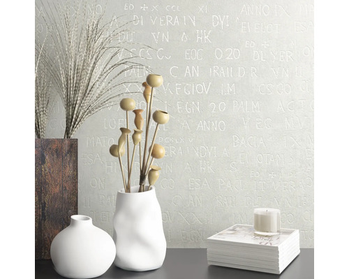 Dekoratives Interieur mit Vasen, Trockenblumen, Buch und Kerze vor einer Wand mit Schriftmuster