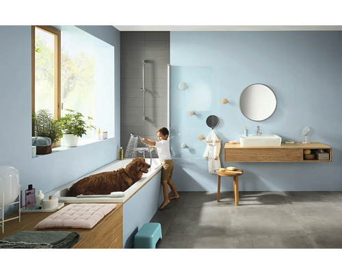 Helles Badezimmer mit Badewanne, Waschtisch, Spiegel und einem Kind, das einen Hund in der Wanne wäscht.