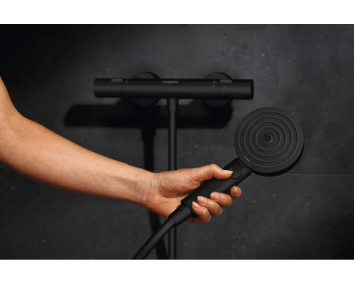 Hand hält Duschkopf vor Thermostatarmatur