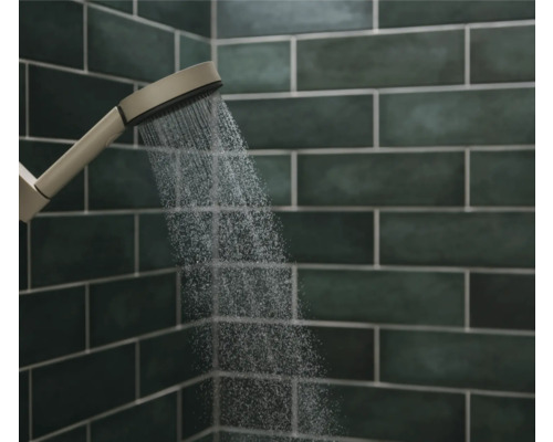 Handbrause mit Wasserstrahl vor einer gefliesten Wand im Badezimmer