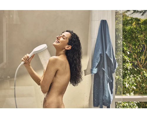 Frau unter der Dusche mit Handbrause und Bademantel im Badezimmer