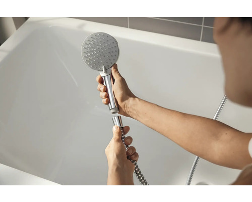 Person montiert einen Duschkopf an einem Duschschlauch vor einer Badewanne.
