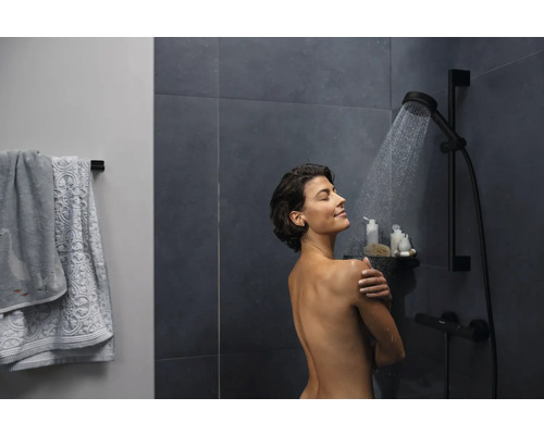 Frau unter einer Dusche mit Brausestange und Handtüchern an der Wand