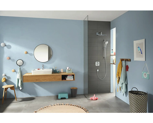 Helles Badezimmer mit Waschbecken, Spiegel, Dusche und verschiedenen Accessoires.