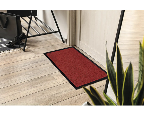 Szene mit einer rechteckigen Fußmatte mit Einfassung, die auf einem Holzboden vor einer Tür liegt.