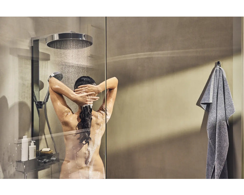 Frau unter der Dusche mit Kopfbrause und Handbrause sowie Duschregal und Handtuch