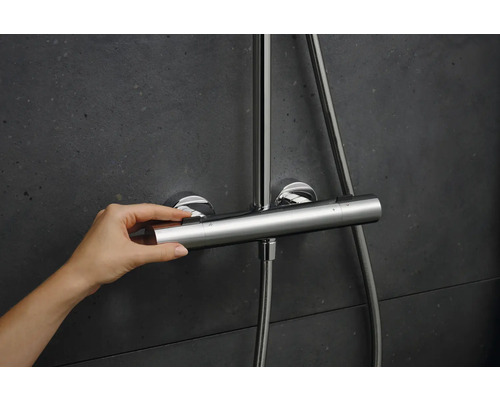 Eine Hand bedient einen Duschthermostat aus Metall an einer Wand.