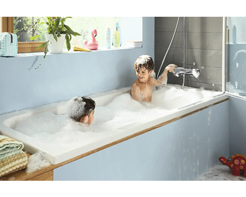 Zwei Kinder spielen mit Badeschaum in einer Badewanne in einem Badezimmer.