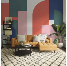 Wohnzimmer mit braunem Sofa, Couchtisch, Regal und Zimmerpflanze vor einer Wand mit geometrischem Muster