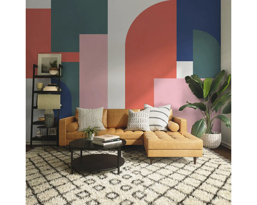 Wohnzimmer mit braunem Sofa, Couchtisch, Regal und Zimmerpflanze vor einer Wand mit geometrischem Muster