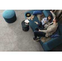Wohnzimmer mit grauen Bodenfliesen, blauem Sofa, Hocker und Beistelltisch