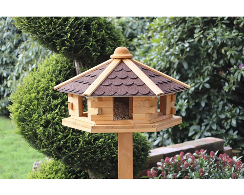 Vogelhaus mit Dach und Futtersilo auf einem Holzpfosten im Garten.