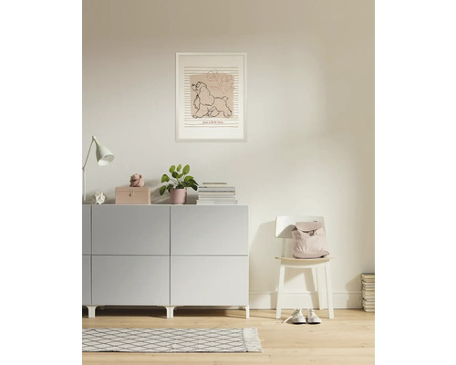 Wohnzimmer mit Kommode, Lampe, Zimmerpflanze, Bilderrahmen und Stuhl mit Rucksack