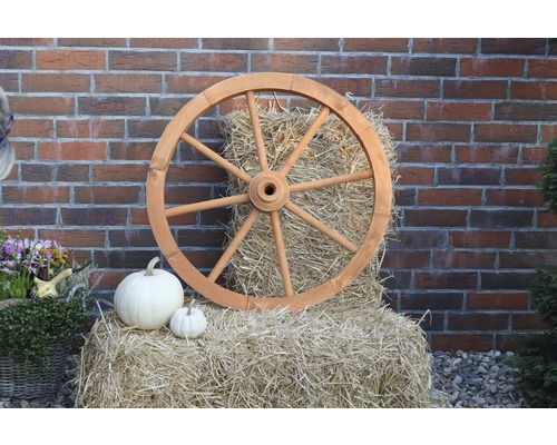 Dekorative Szene mit Holzrad, Heuballen und Kürbissen vor einer Ziegelwand