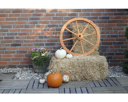 Herbstliche Dekoration mit Kürbissen, Heuballen und Wagenrad vor einer Backsteinmauer
