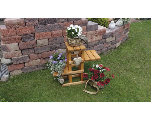 Gartenansicht mit Blumenarrangements und Holzdekoration auf Rasenfläche vor einer Mauer