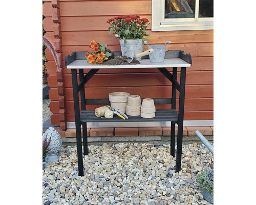 Gartentisch mit Blumen, Töpfen und Gartengeräten vor einem Holzhaus
