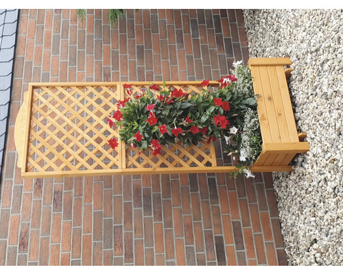 Holzspalier mit Blumenkasten und roten Blumen an einer Backsteinmauer