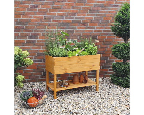 Hochbeet aus Holz mit Kräutern und Gemüse im Garten vor einer Backsteinmauer