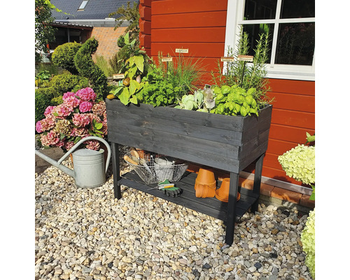 Hochbeet aus Holz mit Kräutern und Gartenzubehör im Garten