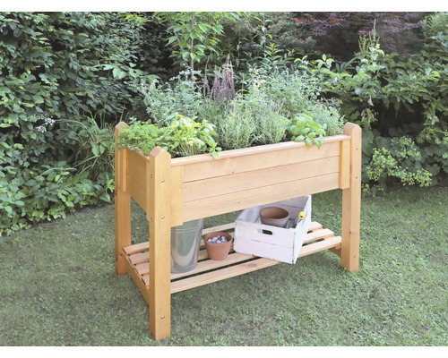 Hochbeet aus Holz mit Kräutern und Gartenzubehör auf einer Rasenfläche