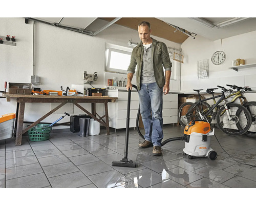 Mann saugt mit einem Nass-Trockensauger Wasser in einer Garage auf