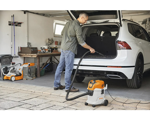 Mann saugt Kofferraum eines Autos mit einem Nass Trockensauger der Marke Stihl
