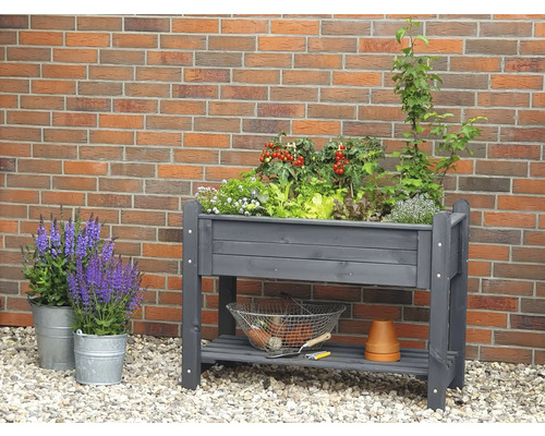Hochbeet aus Holz mit Pflanzen und Gartenzubehör vor einer Backsteinmauer