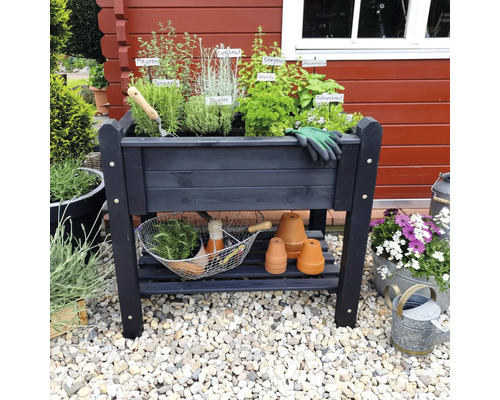 Hochbeet aus Holz mit Kräutern, Gartengeräten und Tontöpfen auf einem Kiesuntergrund