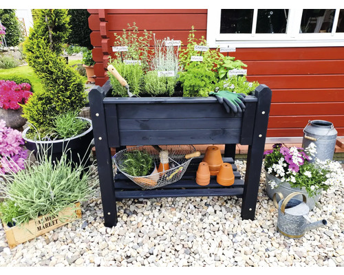 Hochbeet aus Holz mit Kräutern, Gartengeräten und Dekoration vor roter Holzwand