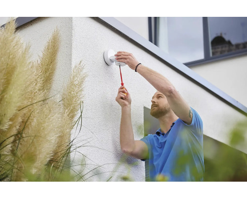 Ein Mann montiert eine Außenleuchte mit einem Schraubenzieher an einer Hauswand.