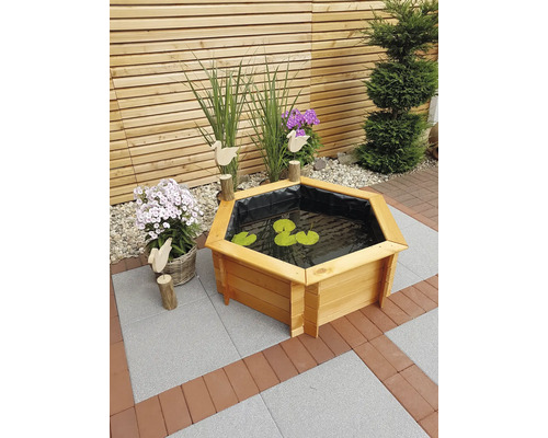 Gartenszene mit Holzterrasse, Pflanzen und einem sechseckigen Hochteich mit Seerosenblättern