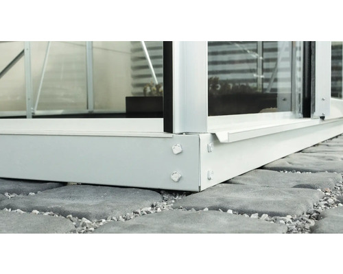 Detailaufnahme einer Gewächshausbasis aus Aluminium auf Steinfliesen.