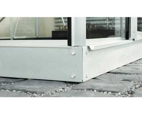 Detailansicht eines Gewächshausfundaments aus Metall auf Pflastersteinen.