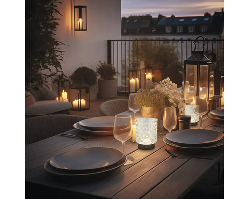 Dekorierter Esstisch im Freien mit Geschirr, Gläsern und batteriebetriebenen Leuchten, die eine gemütliche Atmosphäre schaffen.