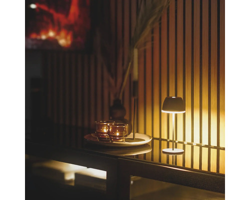 Dekorative Tischszene mit Leuchte, Kerzen und Vase auf einer Anrichte vor einer Holzwand