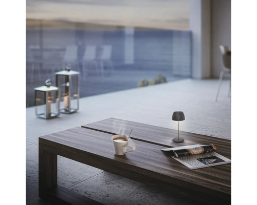 Szene mit Tischleuchte, Tasse, Zeitung und Windlichtern auf einem Tisch im Außenbereich